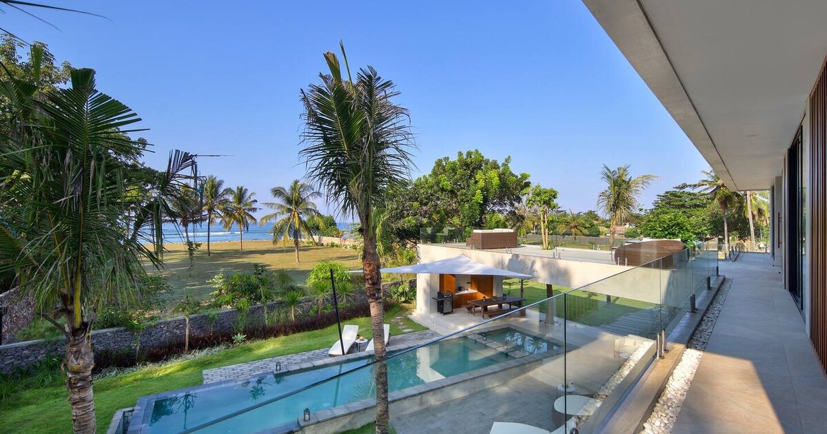 A shaded poolside terrace framed by palms at Wave Lombok, with the South Lombok coast beyond